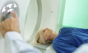 Pacjentka leży w aparacie do tomografii komputerowej. Lekarz przygotowuje badanie, dotykając panelu sterowania. Badanie głowy jest rutynowe, ale warto znać potencjalne skutki uboczne tomografii komputerowej głowy.