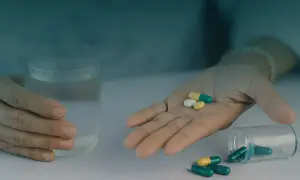 Dłoń z tabletkami i szklanka wody.