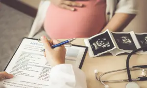 Lekarz wypełnia dokumentację medyczną pacjentki w ciąży, na stole leżą zdjęcia USG płodu i stetoskop. Badanie może wykryć mięśniaki macicy.
