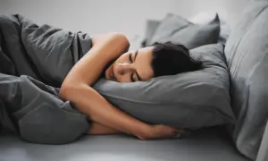Kobieta śpi wtulona w poduszkę. Senność w ciąży to częsty objaw, który wymaga odpoczynku.