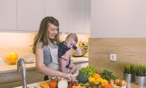 Mama z dzieckiem w kuchni, przygotowuje zdrowe jedzenie. Czosnek i inne warzywa na blacie, idealne dla karmienia piersią.
