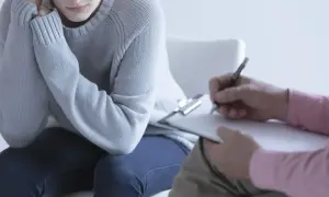 Pacjentka w szarej bluzie rozmawia z terapeutą, który notuje. Dyskutują, czy schizofrenia jest dziedziczna.