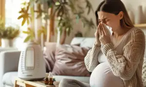 Ciężarna kobieta z chusteczką przy nosie szuka informacji: co na ból gardła w ciąży. Obok nawilżacz powietrza i buteleczki.
