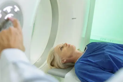 Pacjentka leży w aparacie do tomografii komputerowej. Lekarz przygotowuje badanie, dotykając panelu sterowania. Badanie głowy jest rutynowe, ale warto znać potencjalne skutki uboczne tomografii komputerowej głowy.