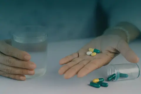 Dłoń z tabletkami i szklanka wody.