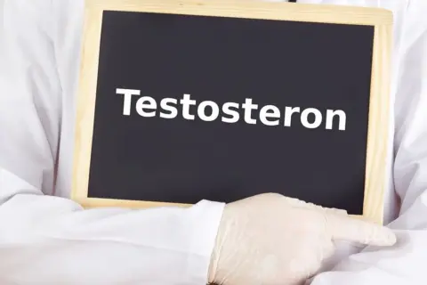 Lekarz w białym fartuchu i rękawiczkach wskazuje na tabliczkę z napisem "Testosteron". Temat: niski testosteron u kobiet.