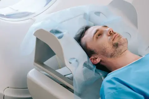 Mężczyzna w niebieskiej koszuli leży na łóżku medycznym pod aparaturą.