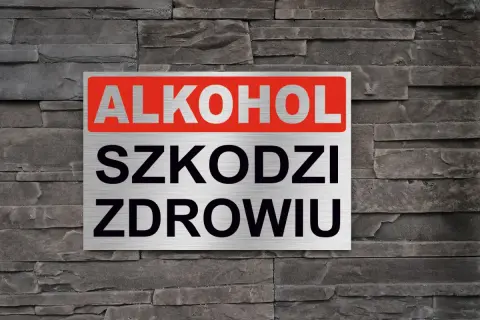 Tabliczka z napisem "ALKOHOL SZKODZI ZDROWIU" na tle kamiennej ściany. Przypomnienie o zagrożeniach.