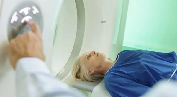 Pacjentka leży w aparacie do tomografii komputerowej. Lekarz przygotowuje badanie, dotykając panelu sterowania. Badanie głowy jest rutynowe, ale warto znać potencjalne skutki uboczne tomografii komputerowej głowy.