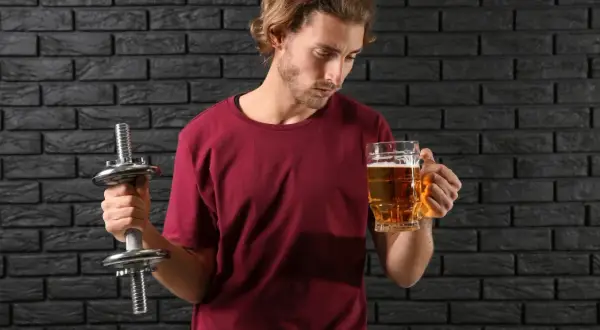Mężczyzna z hantlem zastanawia się, czy piwo bezalkoholowe ma alkohol.