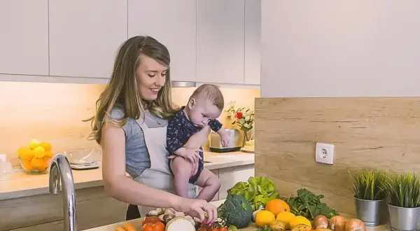 Mama z dzieckiem w kuchni, przygotowuje zdrowe jedzenie. Czosnek i inne warzywa na blacie, idealne dla karmienia piersią.
