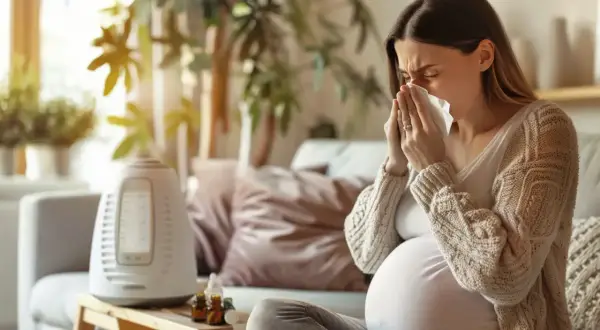 Ciężarna kobieta z chusteczką przy nosie szuka informacji: co na ból gardła w ciąży. Obok nawilżacz powietrza i buteleczki.