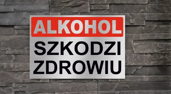 Tabliczka z napisem "ALKOHOL SZKODZI ZDROWIU" na tle kamiennej ściany. Przypomnienie o zagrożeniach.