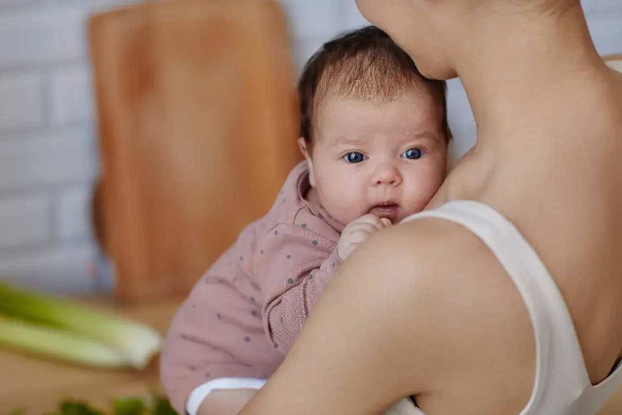 Mama tuli karmić piersią, zastanawia się czego nie jeść przy karmieniu piersią. Na stole seler i zielenina.