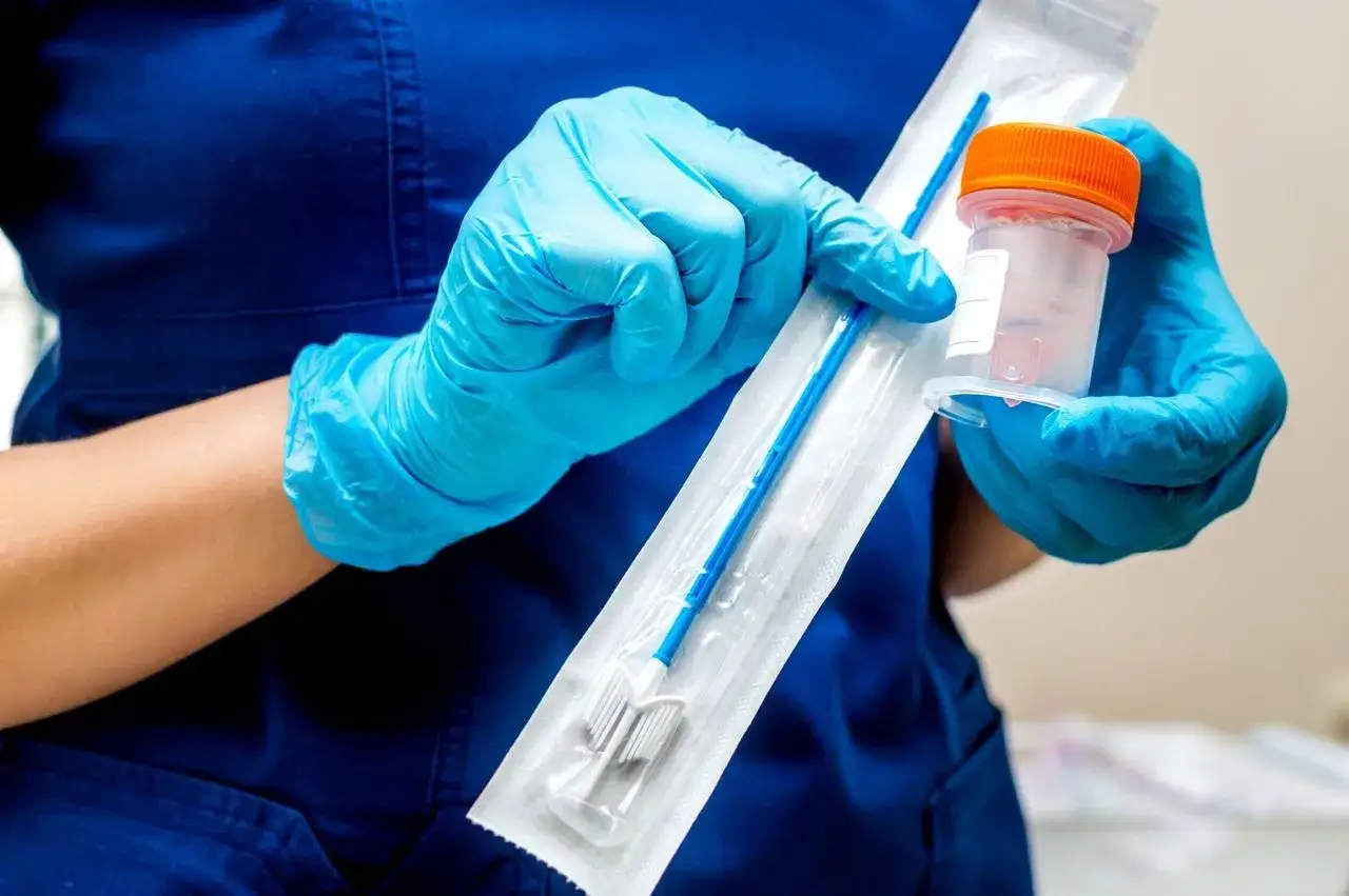 Rękawiczki medyczne trzymają zestaw do cytologii płynnej: szczoteczkę w opakowaniu i pojemnik z płynem.