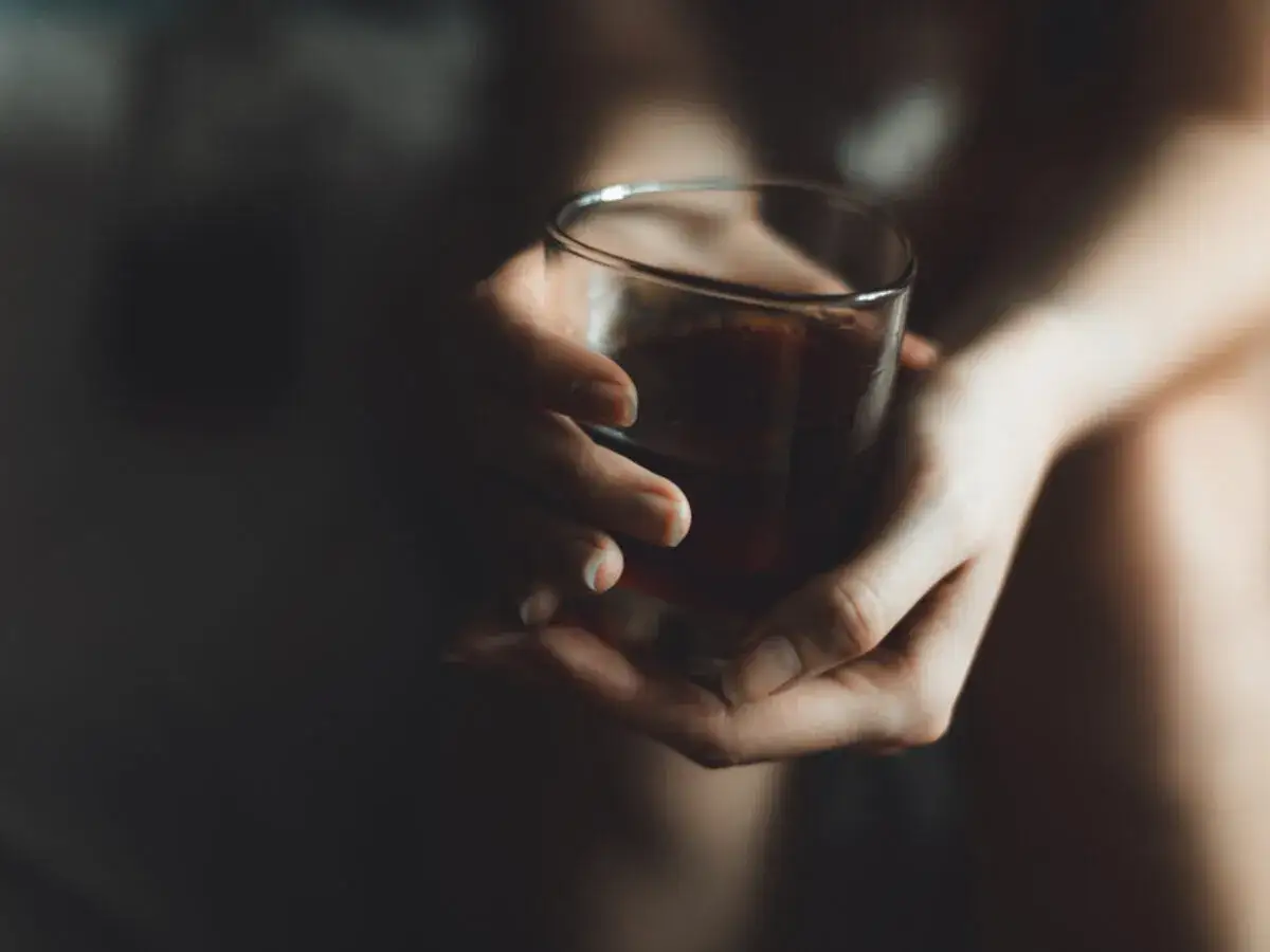 Dłonie trzymają szklankę z ciemnym płynem, rodząc pytanie: czy alkoholizm jest dziedziczny?