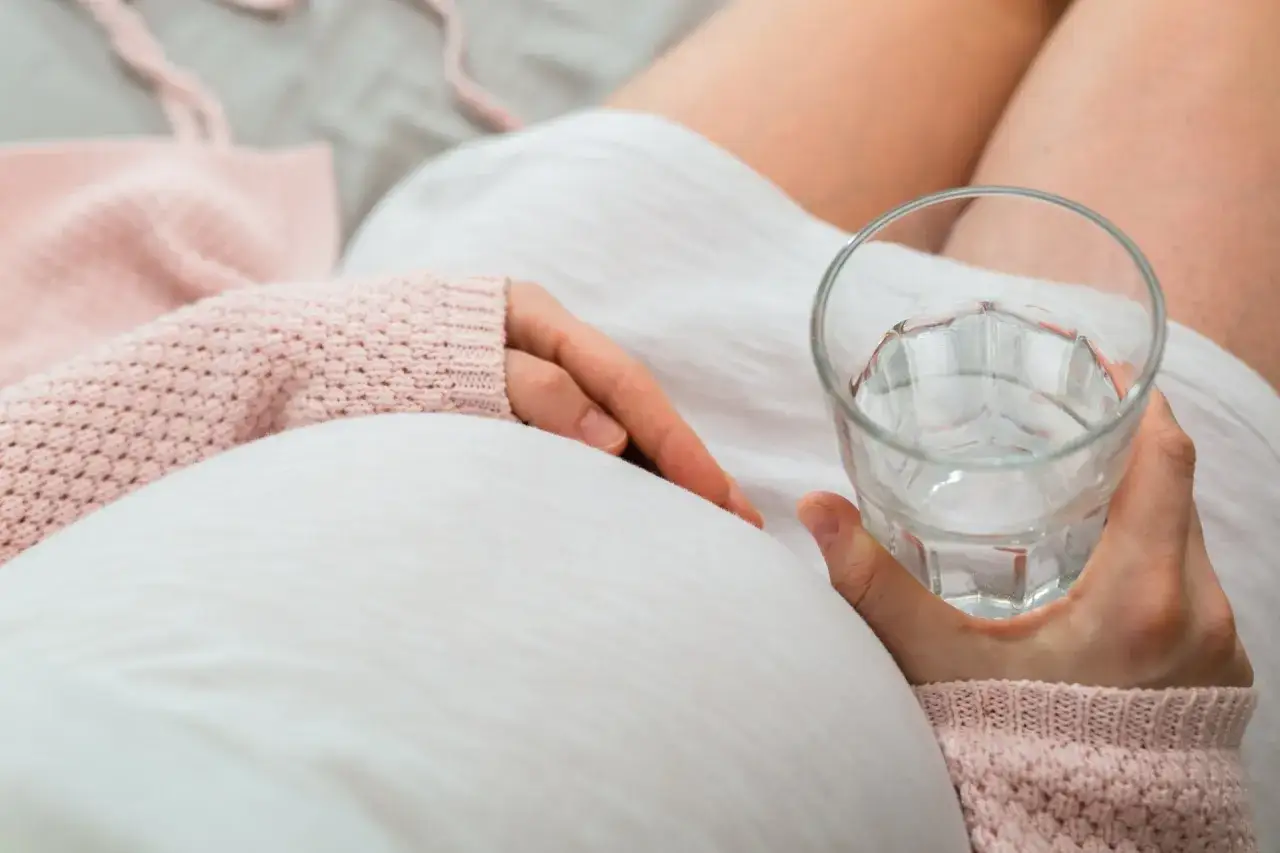 Kobieta w ciąży trzyma szklankę wody, szukając odpowiedzi na pytanie: co na zaparcia w ciąży.