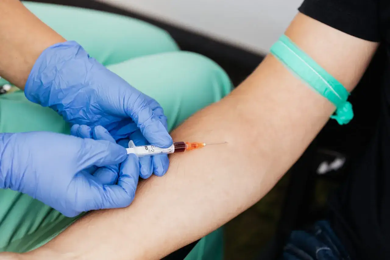 Pielęgniarka w niebieskich rękawiczkach pobiera krew do strzykawki. To ważny etap w diagnostyce, niezbędny do wielu badań z krwi.