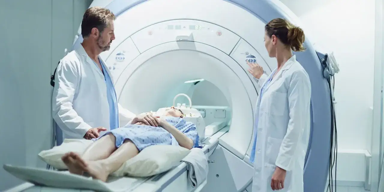 Pacjentka leży w aparacie do rezonansu magnetycznego. Lekarze nadzorują badanie, przygotowanie do rezonansu z kontrastem.