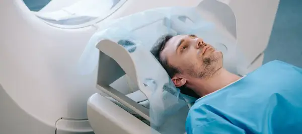 Mężczyzna w niebieskiej koszuli leży na łóżku medycznym pod aparaturą.