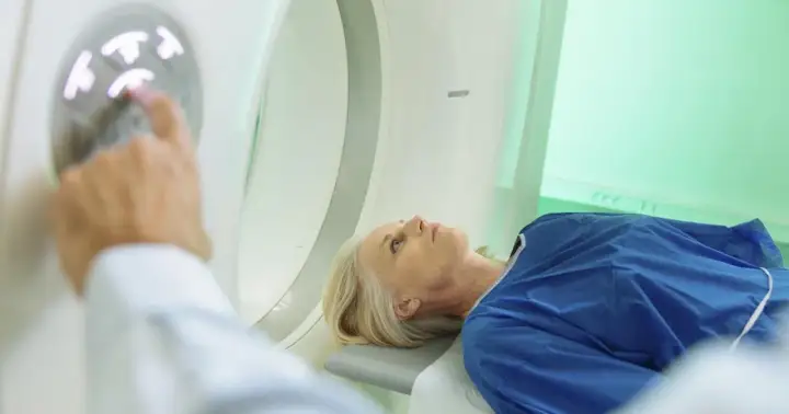 Pacjentka leży w aparacie do tomografii komputerowej. Lekarz przygotowuje badanie, dotykając panelu sterowania. Badanie głowy jest rutynowe, ale warto znać potencjalne skutki uboczne tomografii komputerowej głowy.